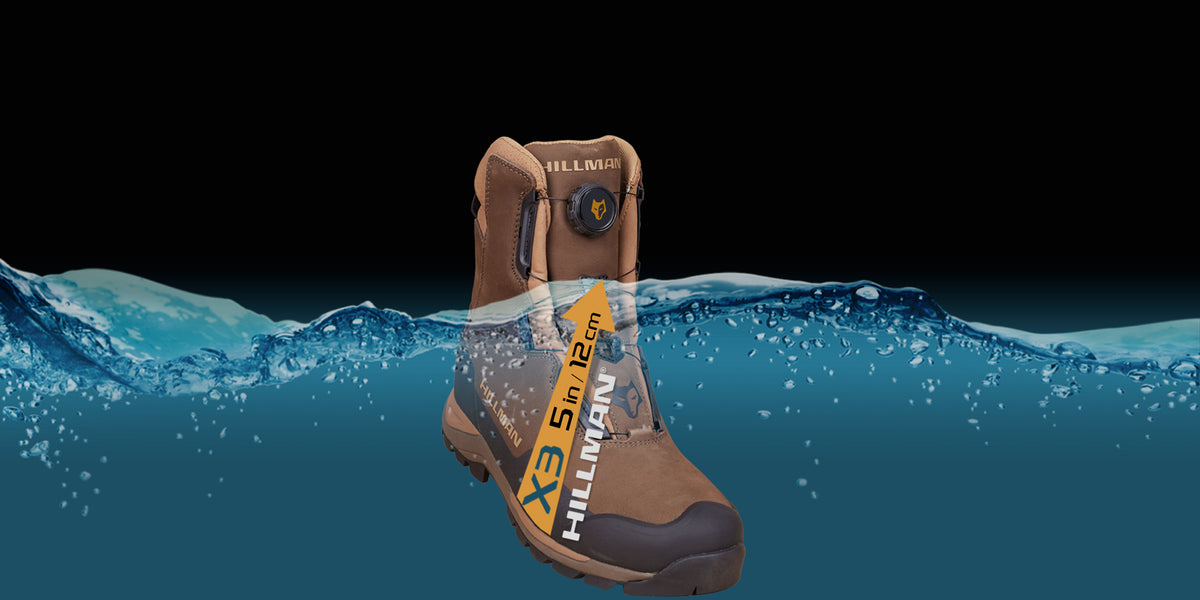 Ein brauner wasserdichter Hillman-Stiefel, der teilweise in Wasser getaucht ist und seine Wasserfestigkeit demonstriert. Der Stiefel hat ein Etikett, das eine Wasserfestigkeit bis zu 5 Zoll oder 12 Zentimetern angibt. Der Hintergrund ist schwarz mit Wasserspritzern.