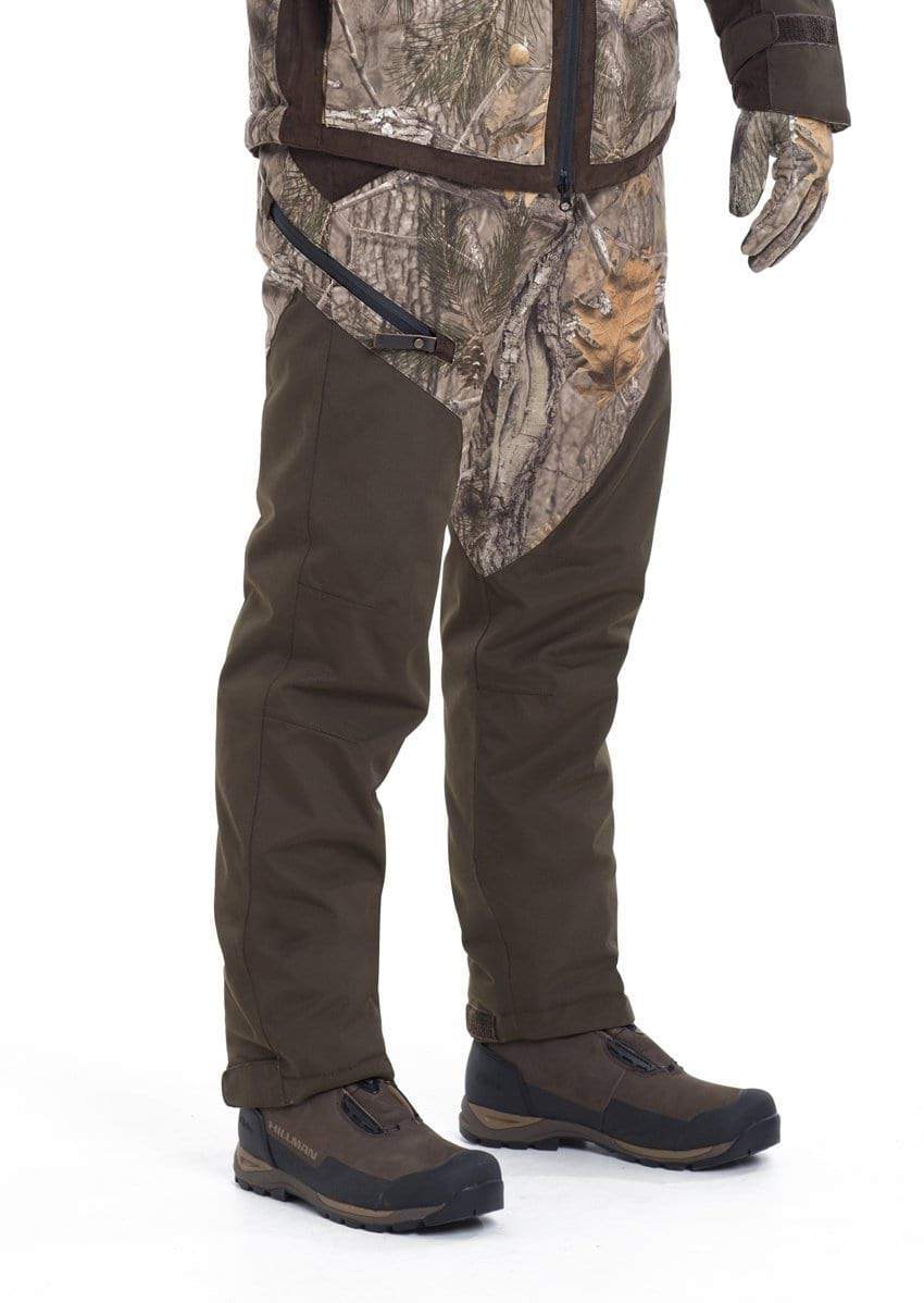 Nur die untere Körperhälfte ist vor weißem Hintergrund sichtbar. Hillmans Jagdhose Fusion Camouflage Winterhose in Grün und Braun mit passenden Handschuhen ist zu sehen. Die Tarnjacke verfügt über eine wasserdichte Atmotec-Membran für optimale Wasserdichtigkeit.