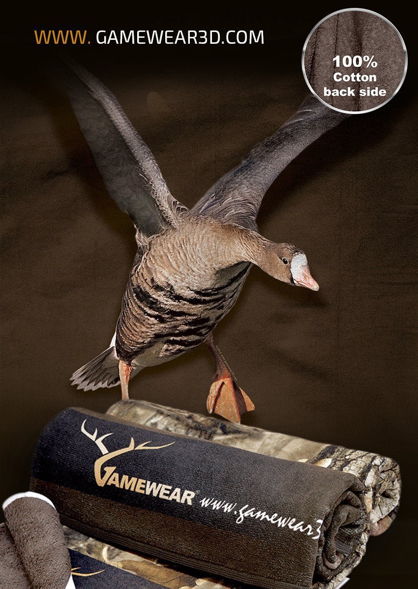 Ein Hillman® Handtuch – 30x50cm Handtuch Blässgans schwebt elegant über einer aufgerollten Tarndecke mit dem „Gamewear“-Logo und „www.gamewear3d.com“. In der oberen rechten Ecke steht „Rückseite 100% Baumwolle“ und verleiht Ihrer Ausrüstung Jagdatmosphäre.