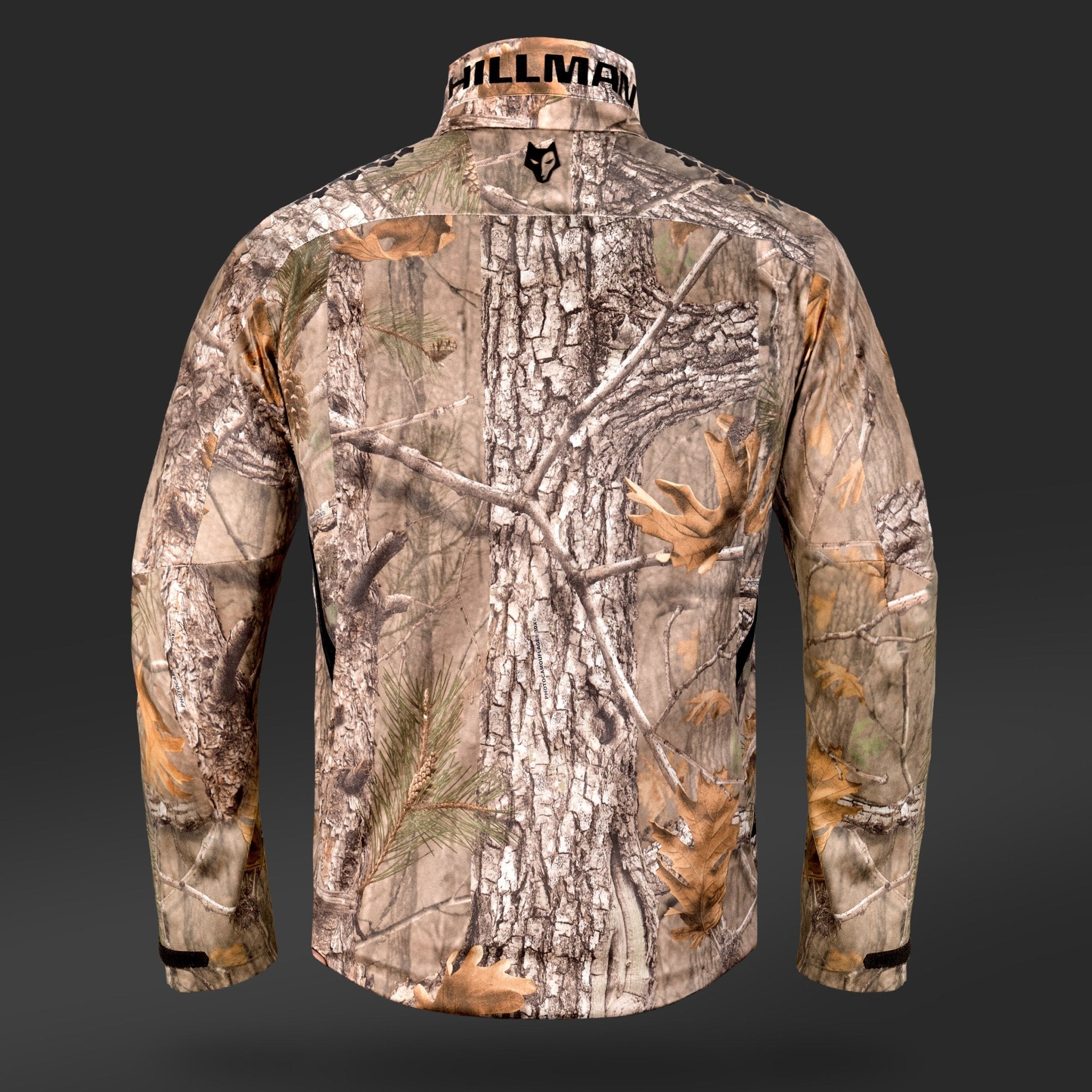 Die Rückansicht der 6OL Winter-Jagdjacke präsentiert ein realistisches Waldmuster mit Baumrinde, Ästen und Blättertarnung. Der Markenname Hillman ist teilweise am Kragen vor einem dunkelgrauen Hintergrund sichtbar.