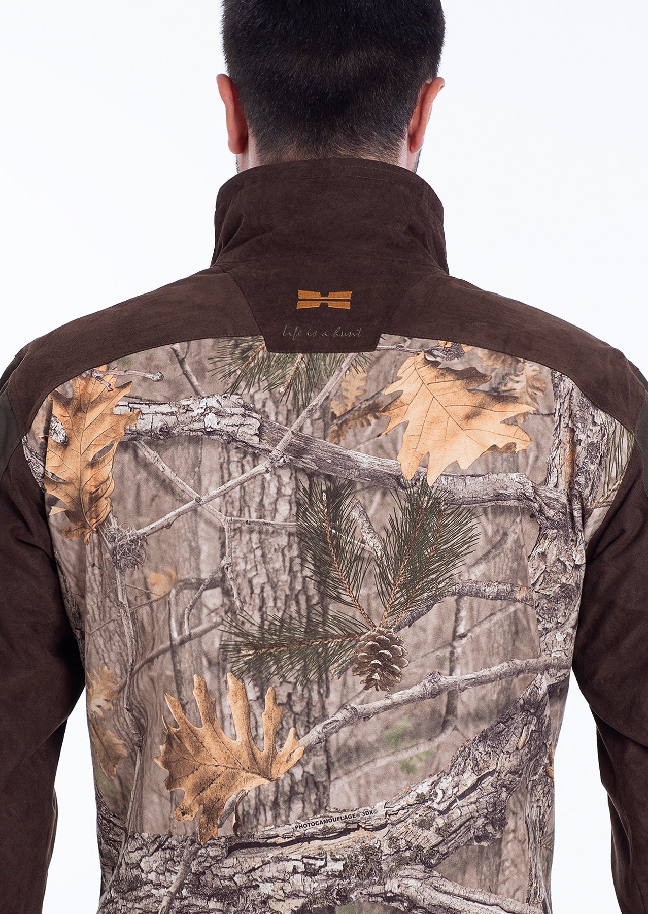 Ein Mann ist von hinten zu sehen, der die Hillman Tarnjacke Jagd | Jagdjacke Camouflage - Fusion 3DX mit braunem Kragen und Schultern trägt; die Rückseite zeigt eine Tarnung aus Baumzweigen, Tannennadeln und Herbstblättern.