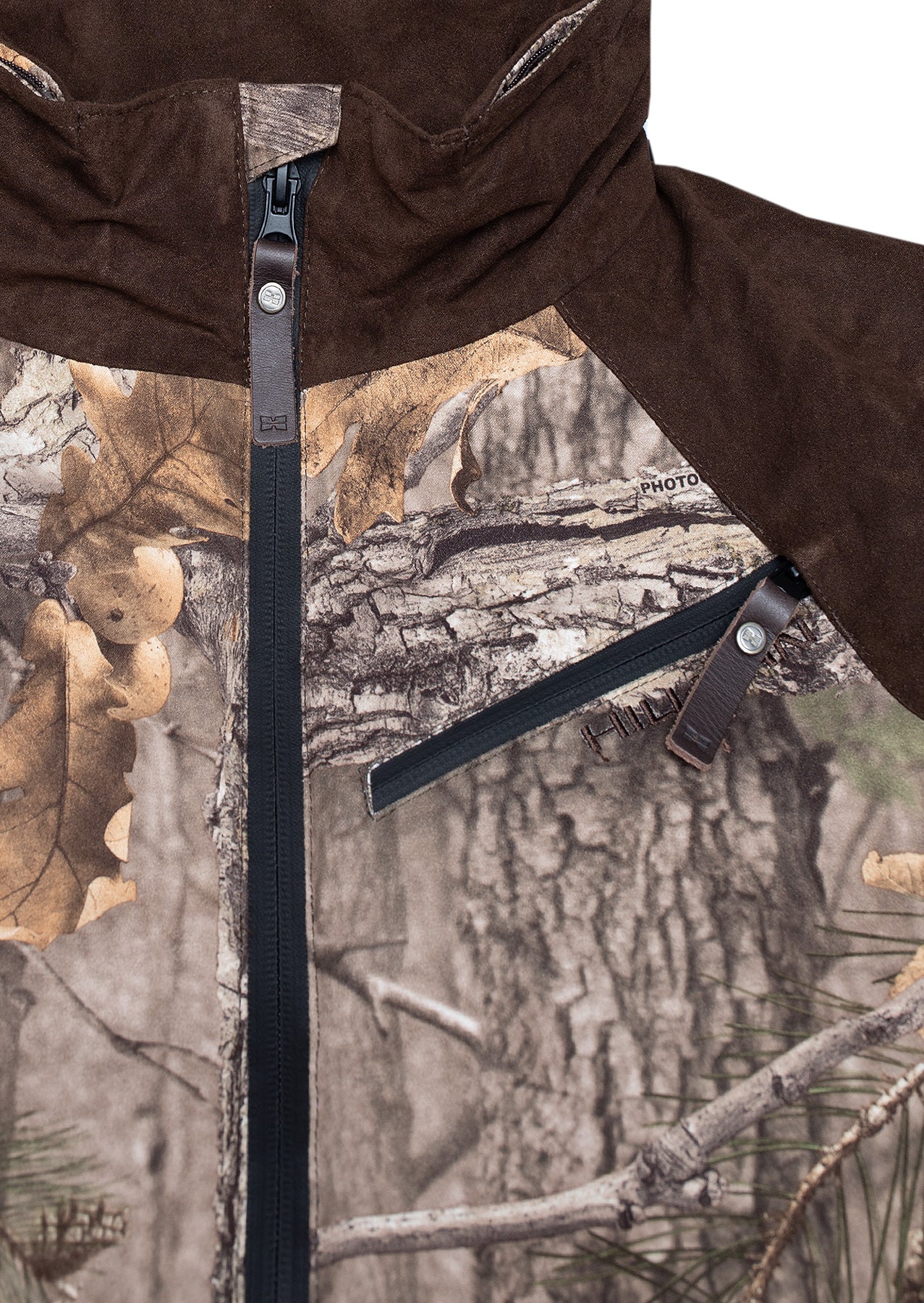 Nahaufnahme der Hillman Tarnjacke Jagd | Jagdjacke Camouflage - Fusion 3DX, mit Waldtarnmuster, braunen wildlederähnlichen Schultern und Kapuze, einem schwarzen Frontreißverschluss und einer diagonalen Reißverschlusstasche mit Lederlasche.