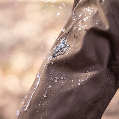 Nahaufnahme eines braunen Ärmels der Hillman 6OL Winter-Jagdjacke, der mit Wasser bespritzt wird. Dabei wird seine wasserabweisende Wirkung deutlich, da die Tropfen abperlen und abrollen. Ein leicht unscharfer Hintergrund betont die Textur und die beeindruckende Wasserfestigkeit des Stoffes.