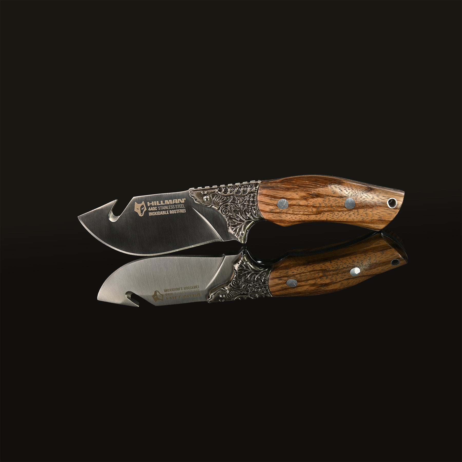 Das Jagdmesser – ARTÉ VON HILLMAN von HILLMAN besticht durch eine Metallklinge mit dem Schriftzug „rostfreier Stahl“ und einen polierten Griff aus Zebrano-Holz mit aufwendigen Metalldetails. Dieses Messer in limitierter Auflage ist vor einem dunklen Hintergrund platziert, dessen Spiegelung darunter sichtbar ist.