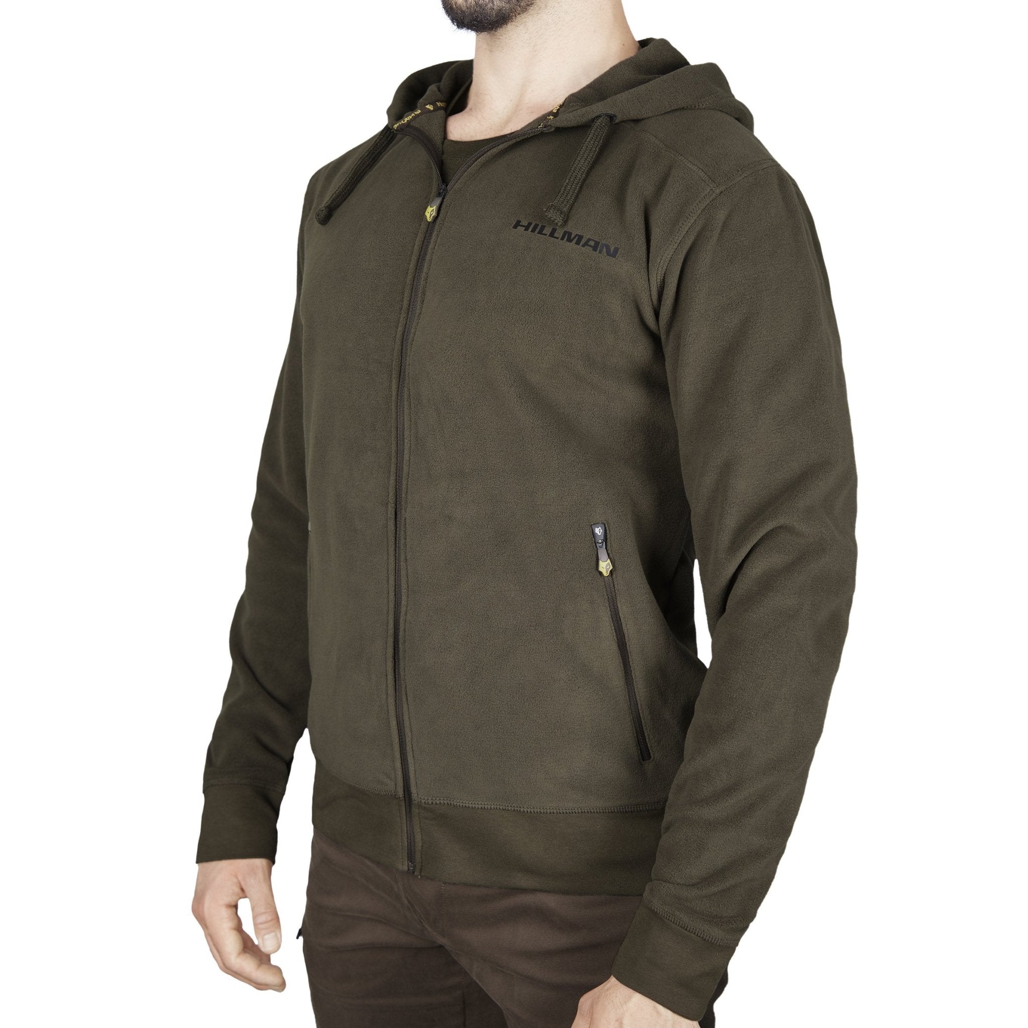 Ein Mann trägt einen olivgrünen Hillman® HOODIE - HOODIE-RUCKSACK mit Reißverschluss und „HILLMAN“-Schriftzug auf der Brust aus warmem Nanofleece-Gewebe. Er verfügt über zwei Reißverschlusstaschen. Der Fokus liegt auf seinem Oberkörper, kombiniert mit einer braunen Hose, die die Details des Kleidungsstücks hervorhebt.