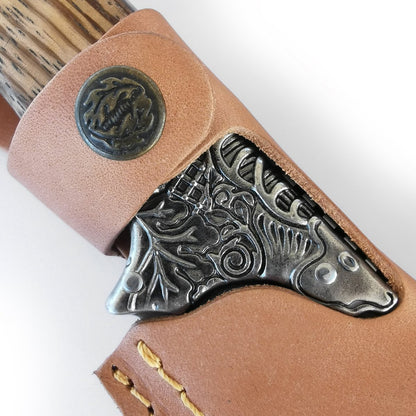 Das Jagdmesser – ARTÉ VON HILLMAN von HILLMAN verfügt über eine dekorative Lederscheide mit aufwendig geprägten Metalldetails, die ein Baum- und Blattdesign präsentieren. Diese limitierte Edition besticht durch genähte Kanten in Zebrano-Holztönen und einen runden geprägten Knopf auf dem Leder.